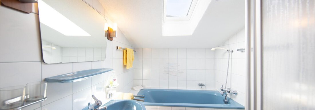 A bathroom with a blue bathtub and sink. Bright tiles and a skylight provide plenty of light. - Haus Alpenstern - Sölden