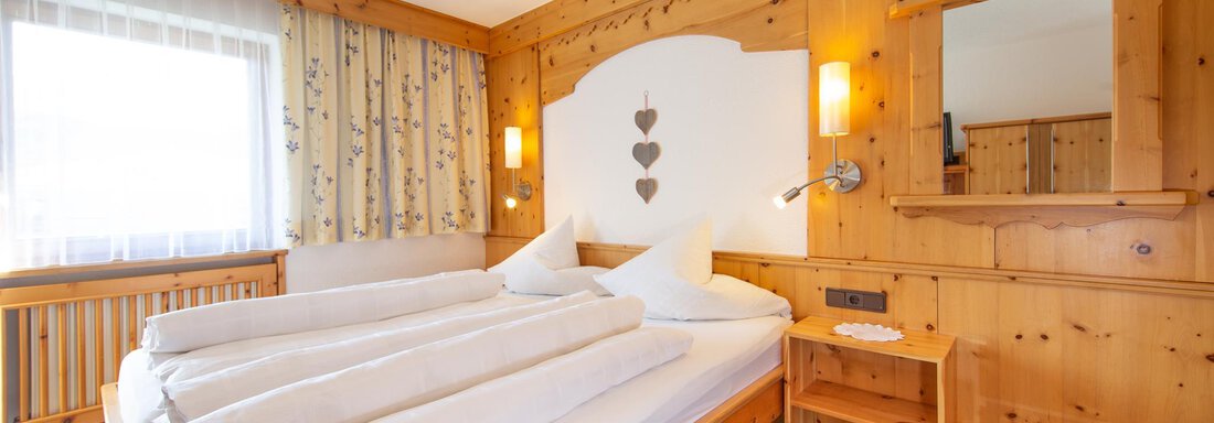 Appt. 4 Doppelzimmer A cozy hotel room with wood paneling and a large window. The room is equipped with a double bed and a small table. - Haus Alpenstern - Sölden
