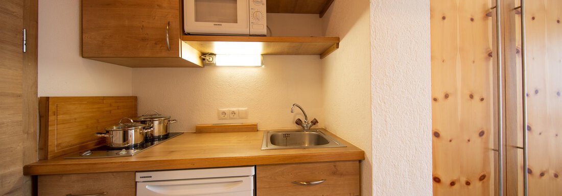 A cozy wooden kitchen with modern appliances. It features a sink, a stove, and a refrigerator. - Haus Alpenstern - Sölden