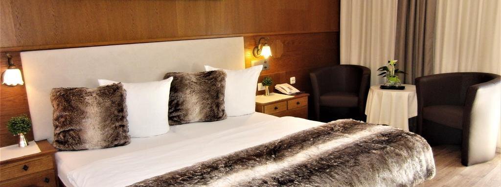 Doppelzimmer A modern bedroom with a large bed and soft pillows. Next to the bed are two cozy armchairs and a small table. - Haus Amaris - Sölden