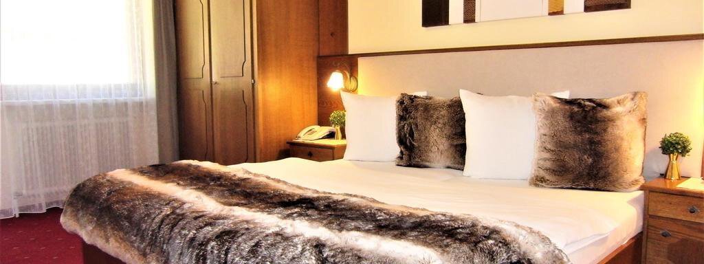 A cozy bedroom with a large bed and a soft, fur-like throw. The gentle lighting and the wood-paneled wall create an inviting atmosphere. - Haus Amaris - Sölden