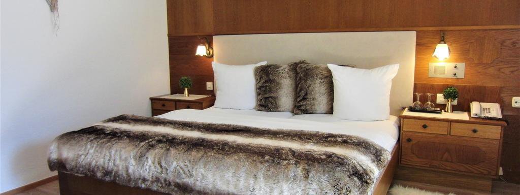 A modern bedroom with a large bed and a cozy comforter. The walls are wood-paneled and there are soft carpets on the floor. - Haus Amaris - Sölden