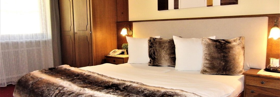 A cozy bedroom with a large bed and a warm blanket. The walls are painted in soft colors, and there is a wardrobe as well as a window with curtains. - Haus Amaris - Sölden