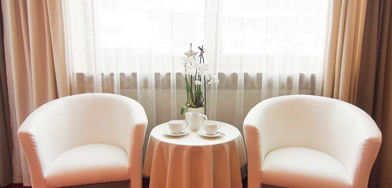 Two white armchairs stand by a small table with two cups. In the background, there is a window with a light curtain and a plant visible. - Haus Amaris - Sölden