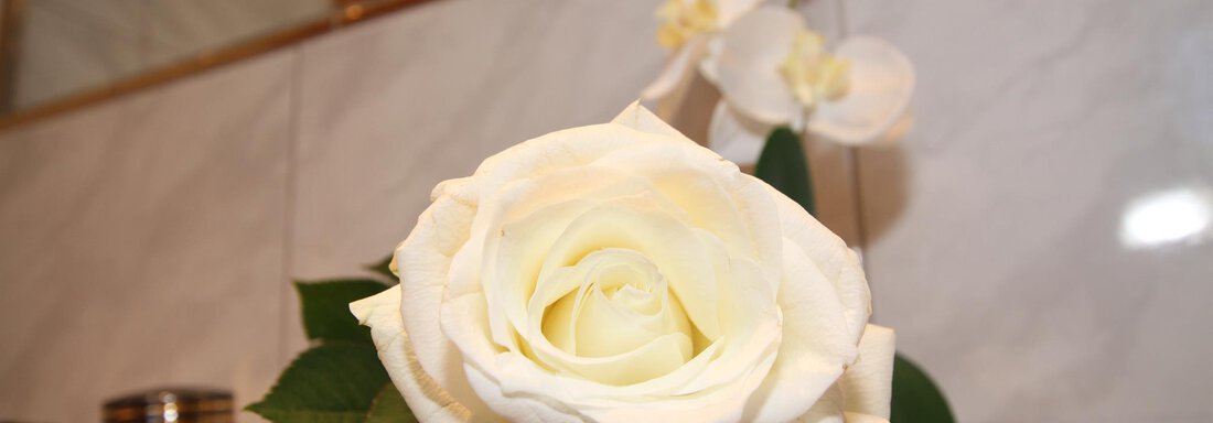 A white rose lies on a gray towel. Floral accents are visible in the background. - Haus Amaris - Sölden