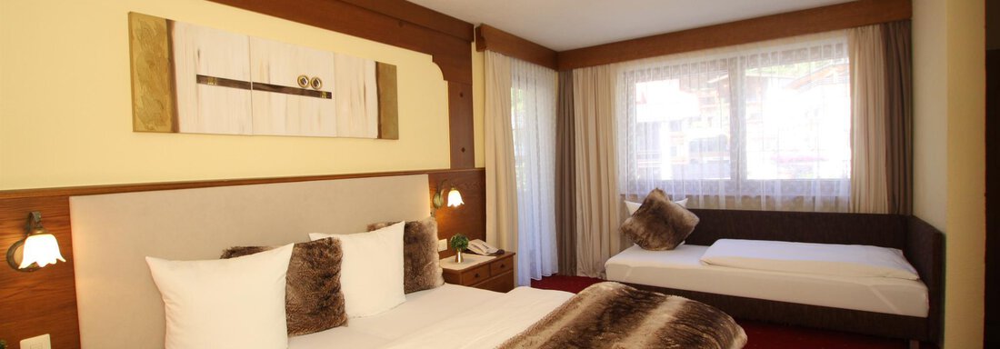 A cozy hotel room with a large double bed and an additional single bed. The room is bright and cheerfully decorated, with a window that lets in daylight. - Haus Amaris - Sölden