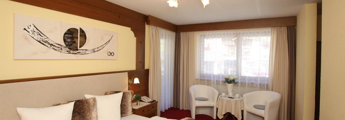 Familienzimmer 2 A comfortable bedroom with a large bed and elegant decoration. Next to the bed are two armchairs and a small table in front of a window with plenty of natural light. - Haus Amaris - Sölden