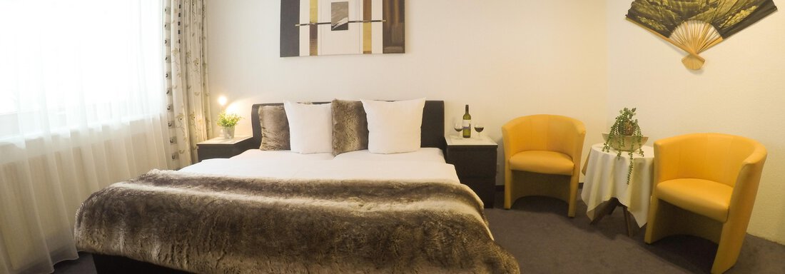A modern hotel room with a large bed and comfortable armchairs.  
Large windows provide plenty of daylight and a pleasant atmosphere. - Haus Amaris - Sölden