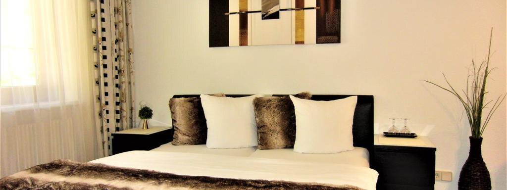A modern bedroom with a large bed and cozy pillows. An abstract artwork hangs on the wall, and a plant stands beside the bed. - Haus Amaris - Sölden