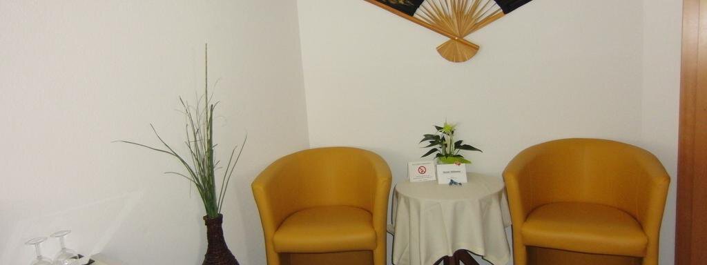 A cozy waiting area with two yellow chairs and a small table. A decorative fan hangs on the wall, and a plant adds inviting ambiance. - Haus Amaris - Sölden