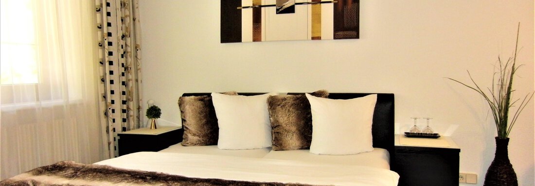 A modern bedroom with a large bed and cozy pillows. The walls are light, and an artistic picture hangs above the bed. - Haus Amaris - Sölden
