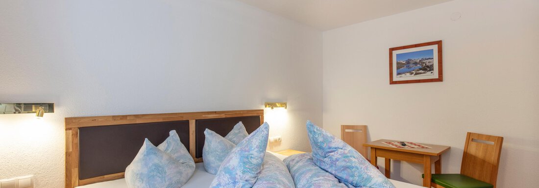 A bright bedroom with a large bed and colorful cushions. A table and a chair are also in the room, along with a picture on the wall. - Haus Bergblick - Sölden
