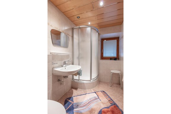 A modern bathroom with a shower cabin and a sink. There is a small window and a stool in the room. - Haus Bergblick - Sölden