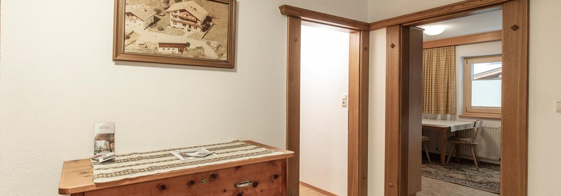 A bright hallway with a wooden dresser and a framed picture on the wall. In the background, two doors leading to other rooms are visible. - Haus Bergblick - Sölden