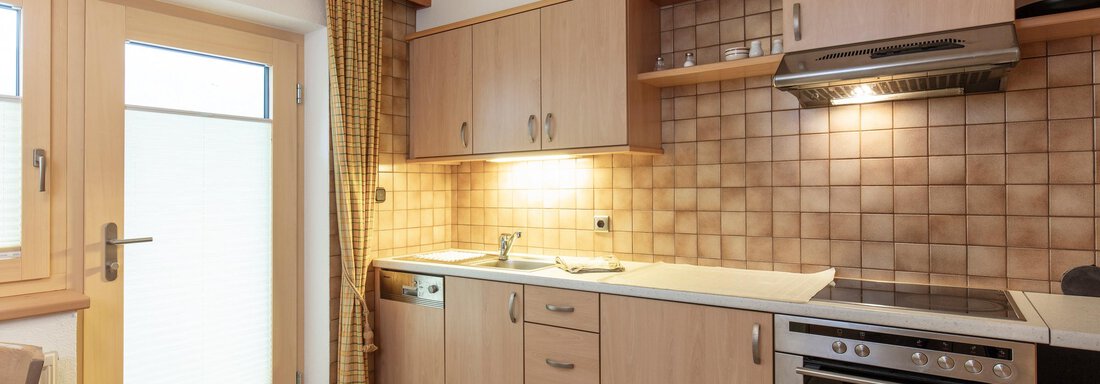 A modern kitchen with wooden cabinets and a bright, inviting atmosphere. The window front ensures plenty of daylight. - Haus Bergblick - Sölden