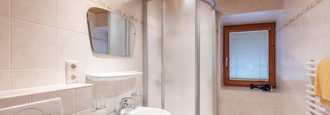 A modern bathroom with a shower, a sink, and a small window. The walls are brightly tiled, and there is a wooden ceiling. - Haus Bergblick - Sölden