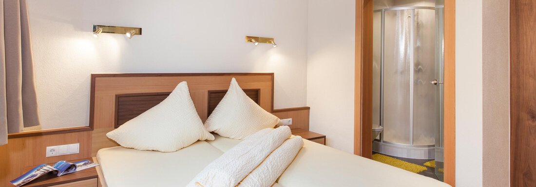 A cozy bedroom with a double bed and two pillows. In the background, there is a shower cabin. - Haus Bergblick - Sölden