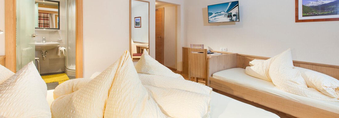 A cozy room with two separate beds and large pillows. In the background, a modern bathroom and a screen are visible. - Haus Bergblick - Sölden
