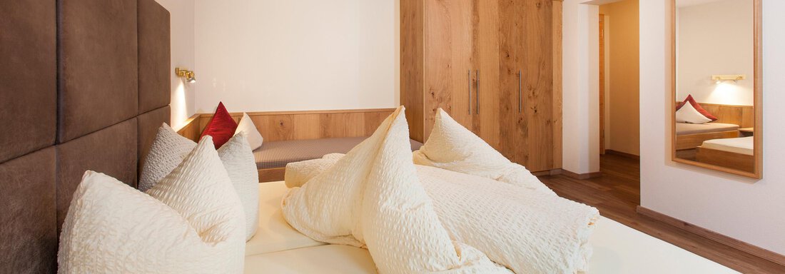A modern bedroom with a large bed and soft pillows. Wooden paneling and a mirrored wall create a warm atmosphere. - Haus Bergblick - Sölden