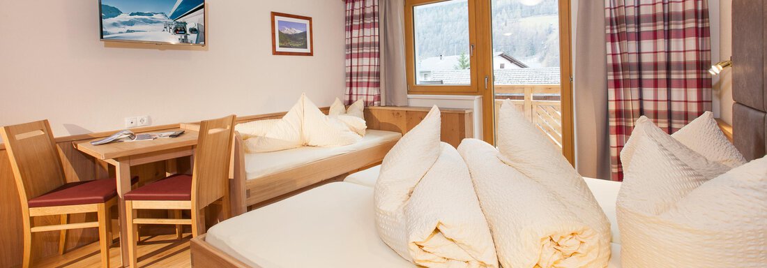 A cozy room with two beds and a table. Large windows provide a view of nature and allow for plenty of daylight. - Haus Bergblick - Sölden