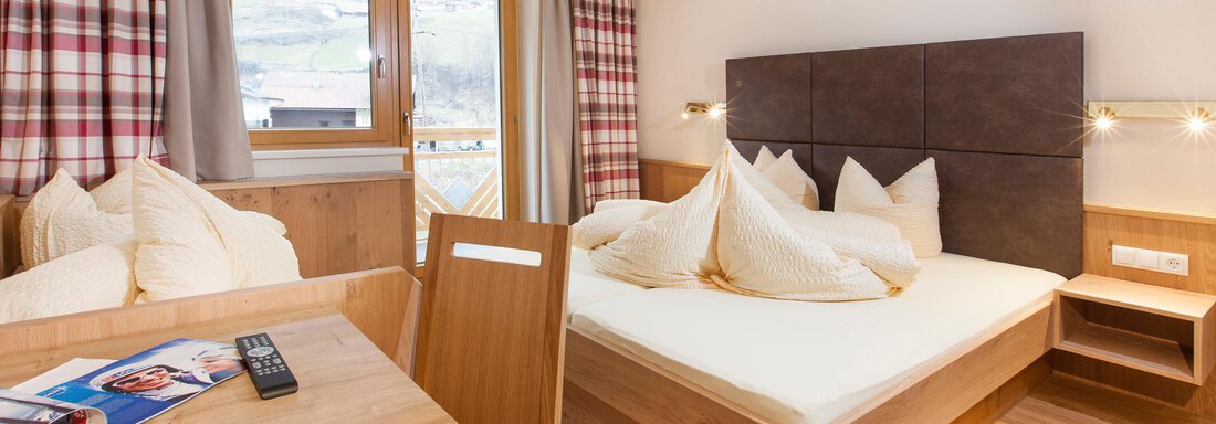 Ötztal A cozy bedroom with a large bed and wood-paneled walls. The room is bright and inviting, with a window that offers a beautiful view. - Haus Bergblick - Sölden