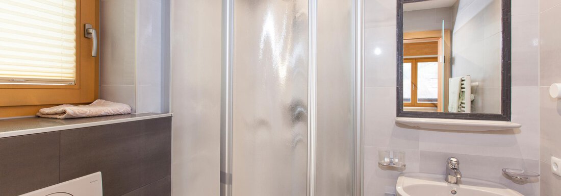 A modern bathroom with a shower cabin and a sink. The room is bright and friendly, with large windows and elegant tiles. - Haus Bergblick - Sölden