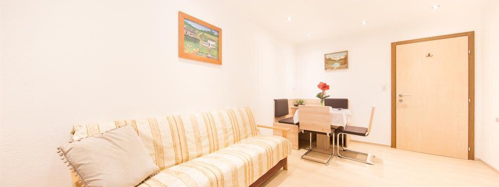 A cozy living room with a striped sofa and a dining area. Pictures hang on the walls, and the room is brightly lit. - Haus Christian - Sölden