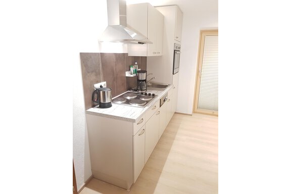 A modern kitchen with bright cabinets and an electric stove. On the countertop, there is a coffee machine and other kitchen appliances. - Haus Christian - Sölden