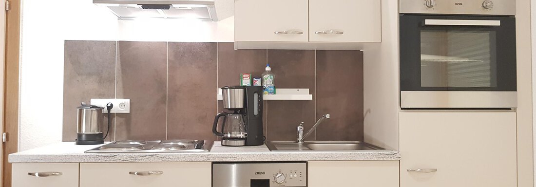 A modern kitchen with white cabinets, a stove, and a dishwasher. The amenities also include a coffee machine and a sink. - Haus Christian - Sölden
