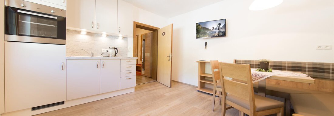 A modern kitchen with white cabinets and wooden flooring. A dining area with a table and chairs is also visible. - Haus Christian - Sölden