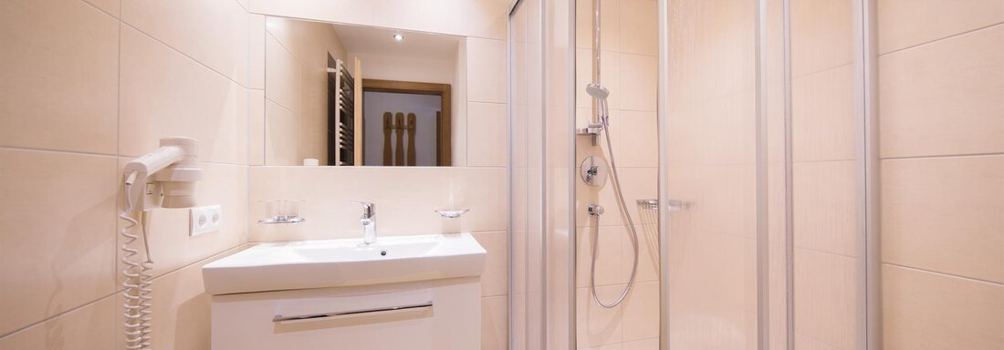 A modern bathroom with a shower and an adjacent sink. The walls are painted in light, neutral colors. - Haus Christian - Sölden