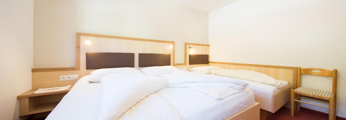 A simple room with two beds and a chair. The walls are light, and the floor is carpeted with red. - Haus Christian - Sölden