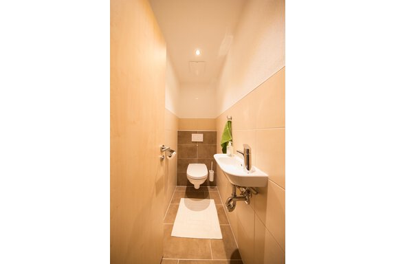 A modern bathroom with light wood and tile-like walls. On display are a toilet, a washbasin, and a towel. - Haus Christian - Sölden