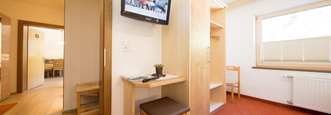 A cozy room with a table, a chair, and a television on the wall. The decor is bright and friendly, with a view of a hallway and a window. - Haus Christian - Sölden
