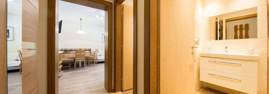 A modern apartment with bright wood surfaces and a bathroom with a sink. In the background, there is a dining area with a table and chairs. - Haus Christian - Sölden