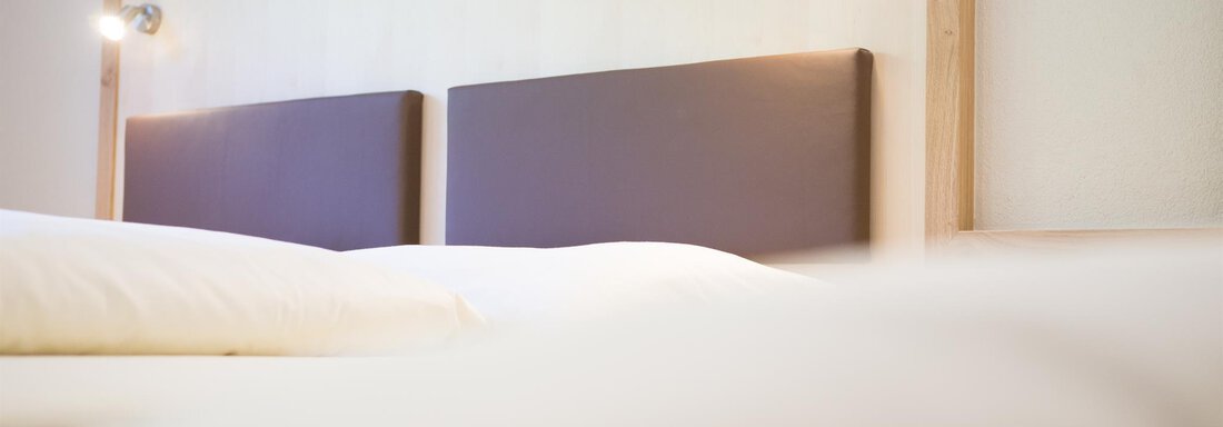 A modern bedroom with a simple headboard and gentle lighting. The bedding is light and inviting. - Haus Christian - Sölden