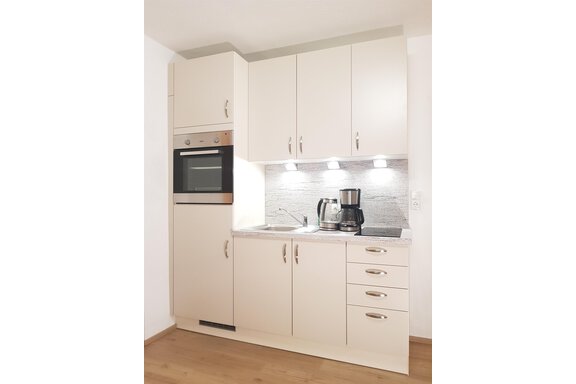 A modern kitchen with white cabinets and a bright countertop. It is equipped with an oven, a sink, and a coffee machine. - Haus Christian - Sölden