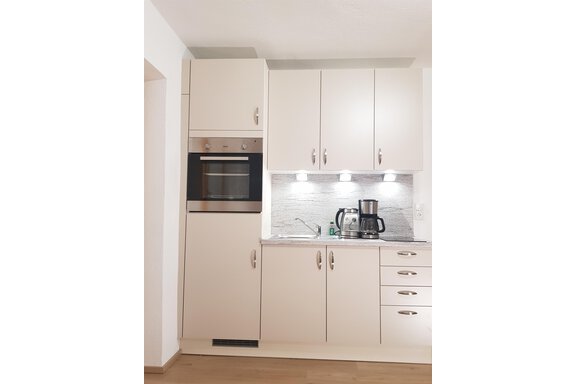 A modern kitchen with white cabinets and an integrated oven. A coffee machine and a sink are also visible. - Haus Christian - Sölden