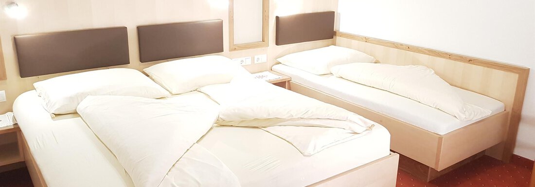 A bright room with two beds and red carpet. The beds are neatly covered with white bedspreads. - Haus Christian - Sölden