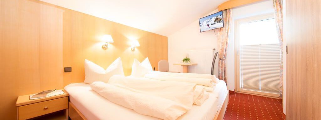 Schlafzimmer 1 A cozy bedroom with two single beds and warm wooden paneling. The room is bright and features a television as well as windows with curtains. - Haus Christian - Sölden