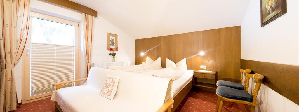 A cozy room with two single beds and wooden decor. By the window are curtains and a small table with chairs. - Haus Christian - Sölden