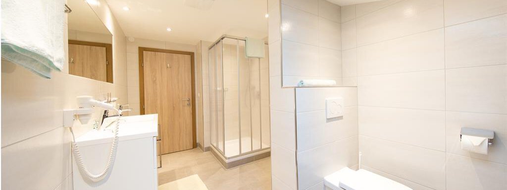 A modern bathroom with a shower, a sink, and a toilet. The walls are light-tiled and the lighting is good. - Haus Christian - Sölden