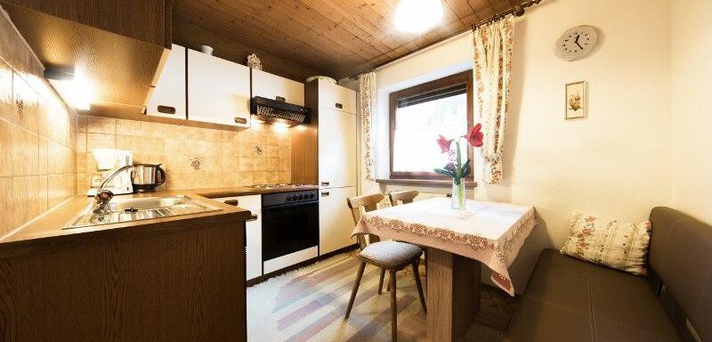 A cozy kitchen with a wooden ceiling and modern equipment. A small table with flowers and a seating area invite you to linger. - Haus Christian - Sölden
