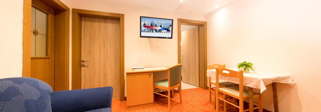 A bright room with a blue sofa, a table and chairs. A television is hung on the wall. - Haus Christian - Sölden