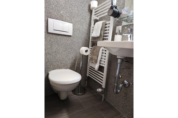 A modern bathroom with a white toilet and a sink. Towels are hanging on the wall, and a towel warmer is installed. - Haus der Bergfreunde - Sölden