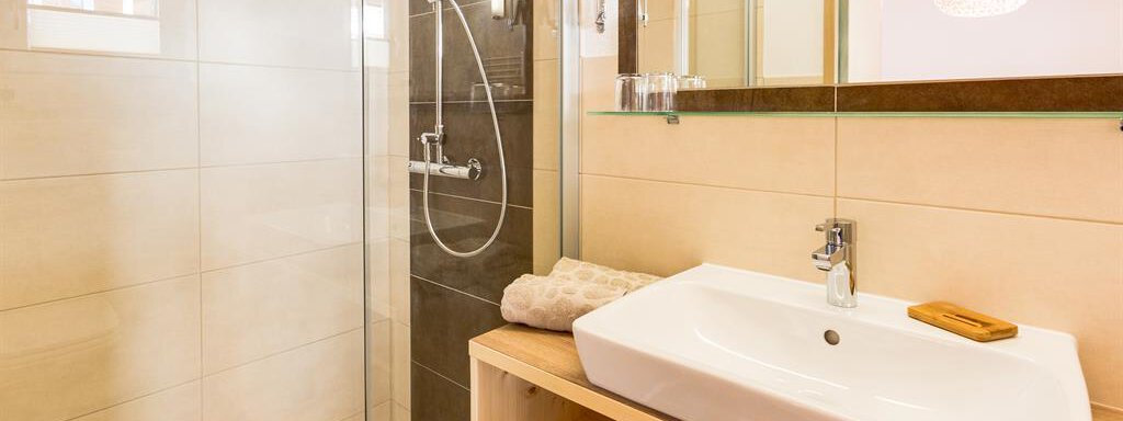 A modern bathroom with a glass shower and a rectangular sink. The walls are painted in soft colors, and there is plenty of light. - Haus Edmund - Sölden