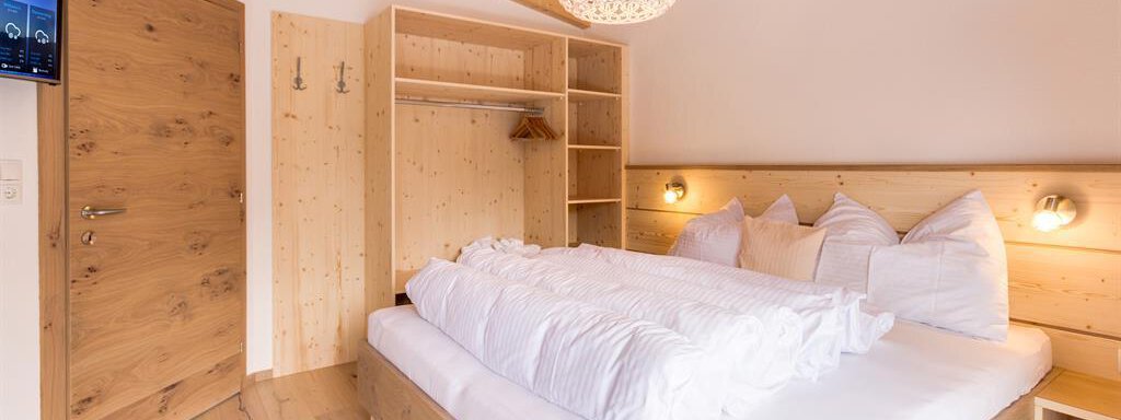 A modern bedroom with wood decor and a large double bed. There is a wardrobe and a television on the wall. - Haus Edmund - Sölden