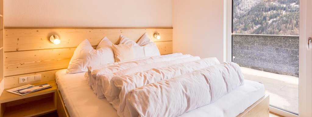 A cozy bedroom with a large bed and bright wooden details. The balcony offers a view of the surrounding mountains. - Haus Edmund - Sölden