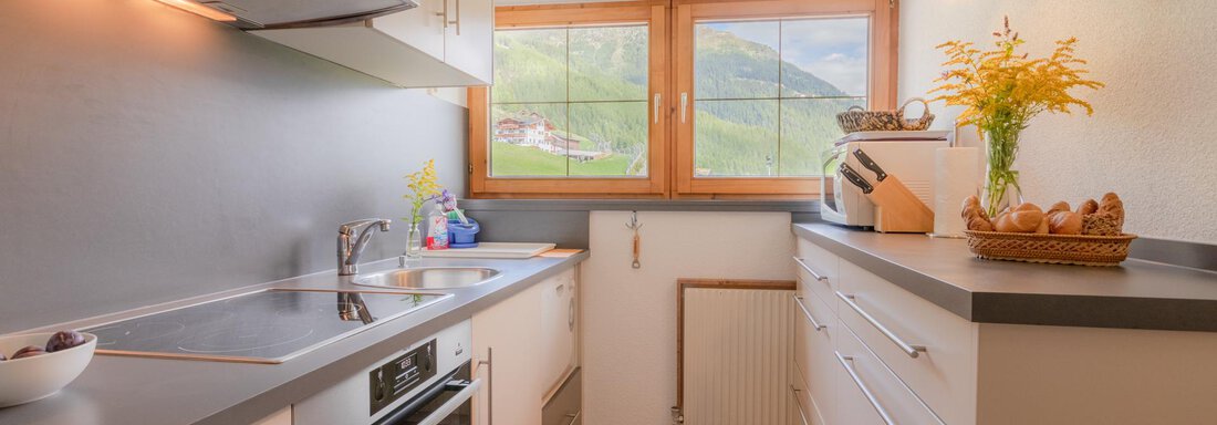 A modern kitchen with bright cabinets and a large window. The room is well-lit and has a warm wooden floor. - Haus Edmund - Sölden