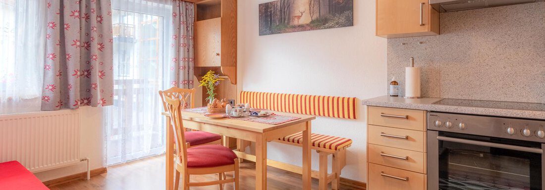 Enzian Küche Haus Edmund A bright kitchen with a wooden table and red chairs. There is a window with curtains and a modern stove. - Haus Edmund - Sölden